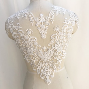 May include: White lace applique featuring floral and vine designs. The lace is beaded and has a delicate, intricate pattern.