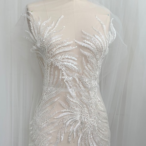 May include: White beaded lace applique with a floral design. The lace is on a mesh backing and is perfect for adding embellishment to a garment.