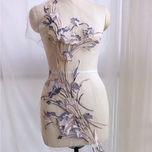 May include: A delicate floral applique with a light brown and purple design on a sheer mesh fabric. The applique features a large flower with smaller flowers and leaves surrounding it. The applique is perfect for adding a touch of elegance to any garment.