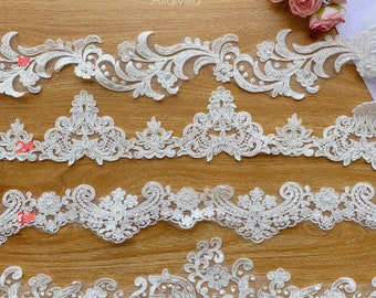 May include: Four different styles of white lace trim with pearl accents. The lace trim is arranged in rows on a wooden surface. The trim is ideal for adding a touch of elegance to any project.