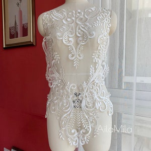 Può includere: Applique in pizzo bianco con un motivo floreale. Il pizzo è delicato e intricato, con una varietà di motivi floreali. L'applique è perfetta per aggiungere un tocco di eleganza a qualsiasi capo.