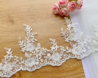 May include: A white lace trim featuring an intricate floral pattern with embroidered leaves and small petals. The lace is embellished with clear beads and sequins that catch the light, set against a sheer mesh base with a scalloped bottom edge.