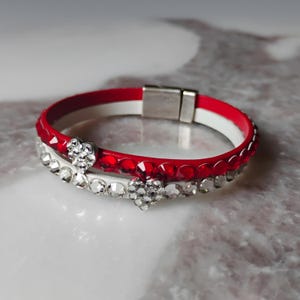 May include: A red and white bracelet with a magnetic clasp. The red band is adorned with red rhinestones. A second white band is embellished with clear rhinestones and two heart-shaped rhinestone accents. Jewelry.