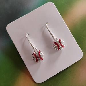 May include: A pair of silver dangle earrings with a red and clear rhinestone baseball charm.
