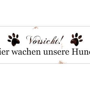 Könnte beinhalten: Weißes Metallschild mit braunen Rostflecken. Das Schild lautet "Vorsicht! Hier wachen unsere Hunde" mit zwei schwarzen Pfotenabdrücken auf beiden Seiten des Textes.