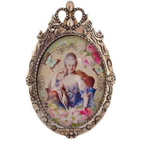 Könnte beinhalten: Ein ovaler, verzierter Bilderrahmen aus goldfarbenem Metall mit einer Glasfront. Der Rahmen hat ein detailliertes Design mit einer Krone oben. Das Bild im Rahmen ist eine Vintage-Illustration einer Frau in einem blauen Kleid mit Blumen und Schmetterlingen.