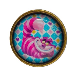 Peut inclure: Un bouton rond de couleur or avec un dessus en verre représentant une image de dessin animé du Chat du Cheshire d'Alice au pays des merveilles. Le chat est rose et violet avec un large sourire et est allongé sur un fond à carreaux bleu et blanc.