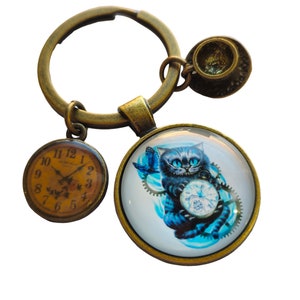 Peut inclure: Un porte-clés en bronze avec un charme rond en verre représentant un Chat de Cheshire bleu tenant une montre de poche. Le charme est entouré d'engrenages et d'un papillon. Le porte-clés comprend également un petit charme en forme de tasse à thé en bronze et un charme rond en forme d'horloge avec des chiffres romains.
