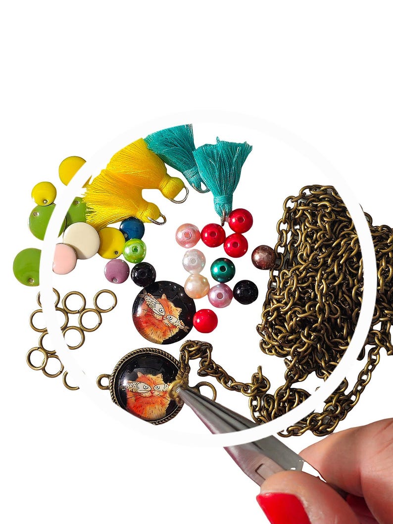 May include: A close-up of a necklace with a cat charm, beads, and a pair of pliers. The necklace is made of a gold chain and the charm is a round glass cabochon with a picture of a cat. The beads are a variety of colours, including red, green, blue, and white.