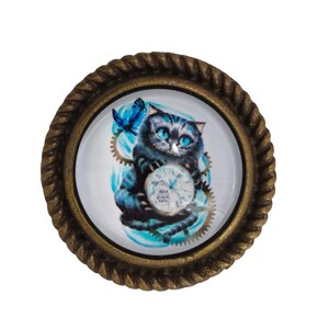 May include: A round, bronze-colored, decorative knob with a glass insert featuring a blue cat holding a pocket watch with gears and a blue butterfly.