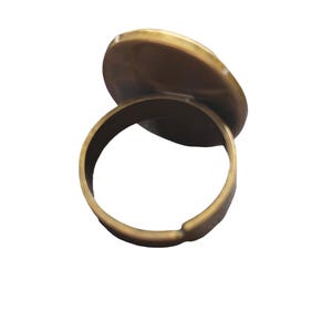 May include: A gold-toned ring with a round, flat top. The ring is open on one side and can be adjusted to fit different finger sizes.