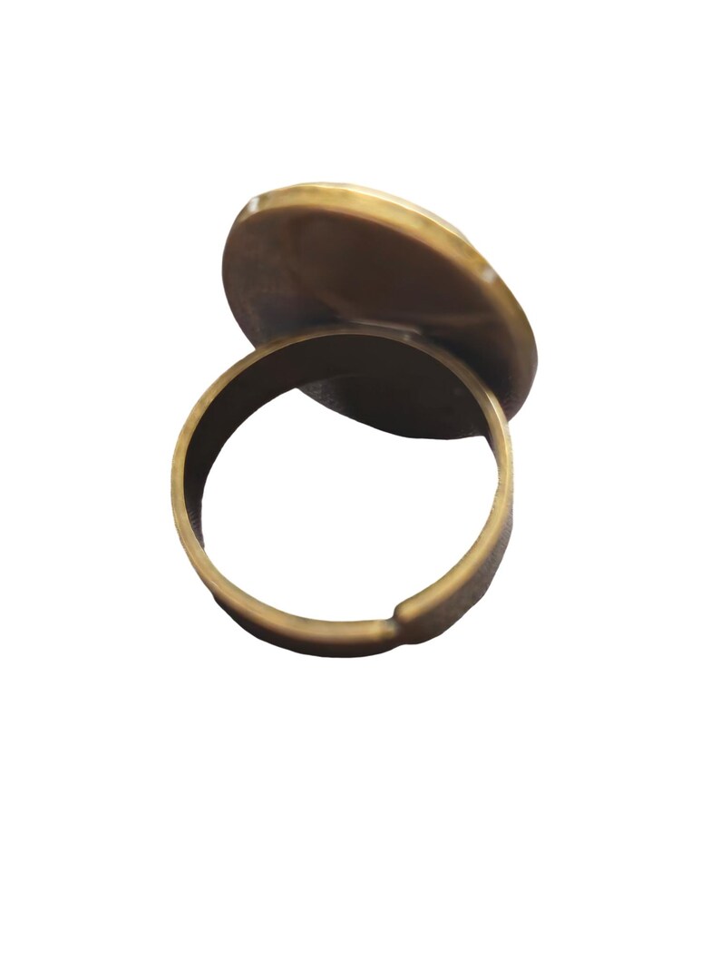 May include: A gold-toned ring with a round, flat top. The ring is open on one side and can be adjusted to fit different finger sizes.