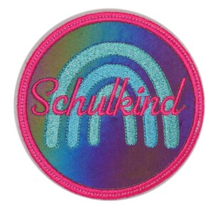 Könnte beinhalten: Ein rosa-blauer gestickter Aufnäher mit einem Regenbogen-Design und dem Text "Schulkid".