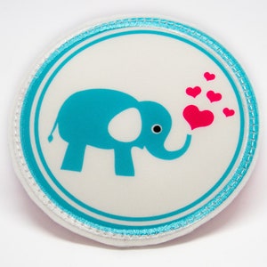 Könnte beinhalten: Ein weißer runder Patch mit einem blauen Rand und einem blauen Elefanten, der rosa Herzen bläst. Der Elefant hat einen weißen Fleck an der Seite.