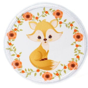 Könnte beinhalten: Ein runder weißer Patch mit einem niedlichen Comic-Fuchs in der Mitte. Der Fuchs ist orange und weiß mit einem buschigen Schwanz. Der Fuchs ist von einem Kranz aus grünen Blättern und orangefarbenen Blumen umgeben.