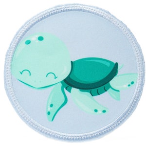 Könnte beinhalten: Ein runder, hellblauer Patch mit einer grünen und hellblauen Comic-Schildkröte mit einem fröhlichen Gesicht. Die Schildkröte schwimmt im Wasser.