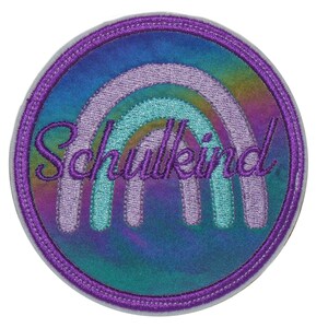 Könnte beinhalten: Runder, regenbogenfarbener Patch mit einem Regenbogen-Design und dem Text "Schulkind" in Lila.