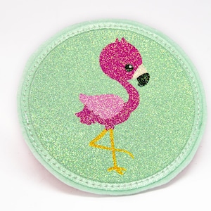 Könnte beinhalten: Ein rosa Flamingo mit gelbem Schnabel und Beinen auf einem grünen Glitzer-Hintergrund. Der Flamingo steht auf einem Bein und hat den Kopf zur Seite gedreht. Der Hintergrund ist hellgrün mit einem glitzernden Finish.
