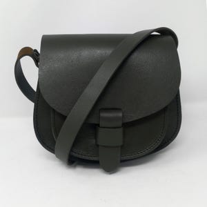 May include: A dark green leather saddlebag with a flap closure and adjustable shoulder strap. The bag has a rounded shape and a buckle detail on the front. The bag is made of a textured leather material.