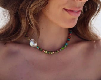 May include: A woman wearing a light blue off-the-shoulder top with a floral print. The top has a ruffled neckline and features a small, white pearl on a multi-colored beaded necklace.