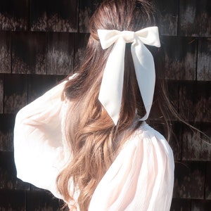 May include: A white satin ribbon tied in a bow, worn in a woman's hair.