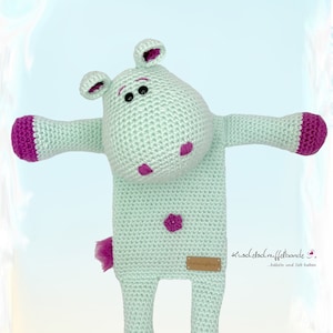 May include: A light blue crocheted hippopotamus toy with pink accents. The hippopotamus has a small pink heart on its belly and a pink tail. The toy is made by "kuschel-elfchen.de/fellbande".