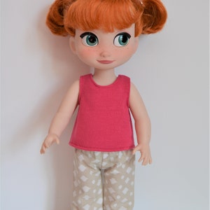 Puede incluir: Una mu&ntilde;eca de pelo rojo que lleva una camiseta rosa sin mangas y pantalones beige con un estampado geom&eacute;trico blanco. La mu&ntilde;eca tiene ojos verdes y pecas.