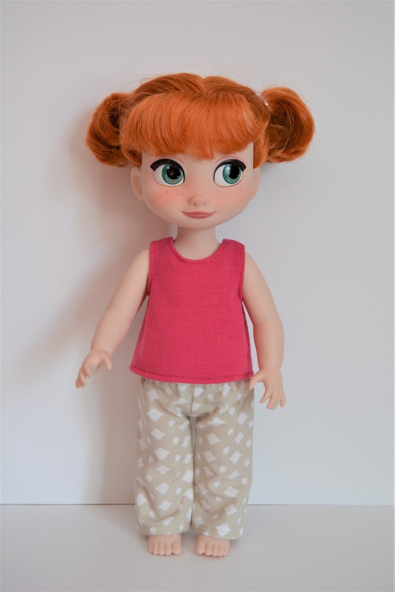 Puede incluir: Una mu&ntilde;eca de pelo rojo que lleva una camiseta rosa sin mangas y pantalones beige con un estampado geom&eacute;trico blanco. La mu&ntilde;eca tiene ojos verdes y pecas.