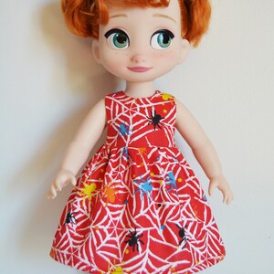 May include: A red dress with a spiderweb and spider print. The dress is sleeveless and has a gathered skirt. The doll is wearing the dress and has red hair.
