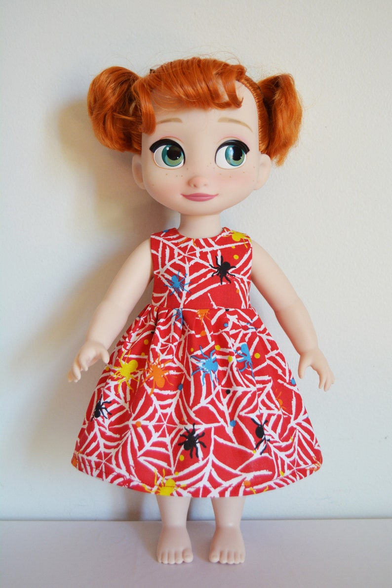 May include: A red dress with a spiderweb and spider print. The dress is sleeveless and has a gathered skirt. The doll is wearing the dress and has red hair.
