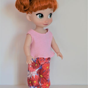 Puede incluir: Una mu&ntilde;eca de pelo rojo que lleva una camiseta rosa sin mangas y pantalones de estampado floral. La mu&ntilde;eca tiene ojos verdes y un lazo negro en el pelo.