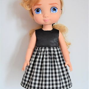 May include: A doll with blonde curly hair wearing a black and white gingham dress with a black satin bodice. The doll is wearing black shoes.