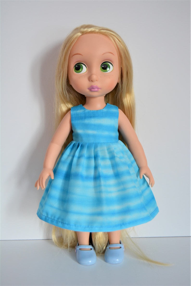 May include: A doll with long blonde hair wearing a blue and white striped dress and blue shoes.