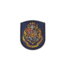 May include: A blue and gold embroidered patch featuring the Hogwarts crest. The crest includes a lion, eagle, badger, and snake, with the words "Draco Dormiens Nunquam Titillandus" around the outside.