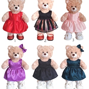 May include: Six plush teddy bears wearing different colored dresses. The bears are all wearing white shoes. The dresses are red, black and white striped, pink, purple, black, and teal.