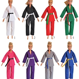 May include: Eight Barbie dolls wearing different coloured karate uniforms with matching belts. The uniforms are white, black, red, green, pink, purple, grey, and blue. Each doll has blonde hair and is wearing a white belt.