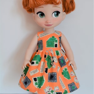 May include: A red-haired doll wearing a sleeveless orange dress with a green and white print. The dress has a variety of text on it, including "naive amorous", "buttons falling", and "funny little house". The doll is wearing black shoes.