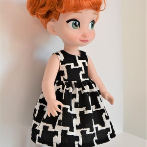 May include: A red-haired doll wearing a black and white geometric print dress and black shoes. The doll has green eyes and a sweet expression.