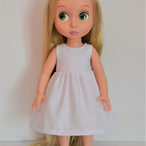 May include: A doll with long blonde hair wearing a white dress with a small pattern and light blue shoes.