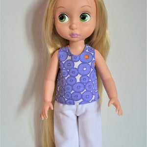 Puede incluir: Una mu&ntilde;eca con el pelo largo y rubio que lleva un top morado sin mangas con c&iacute;rculos blancos y un pantal&oacute;n blanco.
