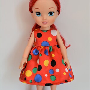 May include: A red and white polka dot dress with colorful polka dots on a doll with red hair and blue eyes.