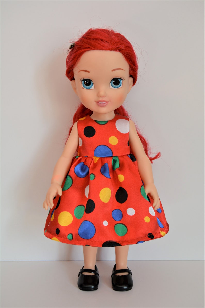 May include: A red and white polka dot dress with colorful polka dots on a doll with red hair and blue eyes.