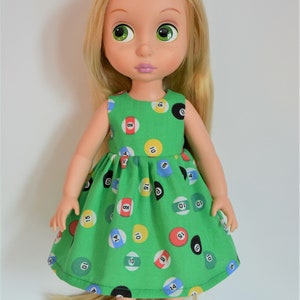 May include: A doll with long blonde hair wearing a green dress with a pattern of colorful billiard balls. The doll is wearing blue shoes.