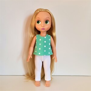 Puede incluir: Una mu&ntilde;eca con el pelo largo y rubio que lleva un top sin mangas de lunares verdes y blancos y pantalones blancos.