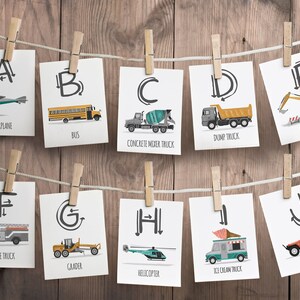 May include: A set of 10 flashcards featuring the alphabet with illustrations of vehicles. Each card has a letter, a vehicle illustration, and the name of the vehicle. The vehicles include an airplane, bus, concrete mixer truck, dump truck, excavator, fire truck, grader, helicopter, ice cream truck, and jeep.