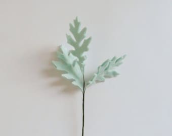 May include: A single stem of artificial greenery with three light green leaves. The leaves are shaped like oak leaves.