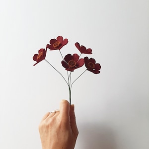 Könnte beinhalten: Ein Strauß aus sechs burgunderfarbenen Filzblumen mit braunen Zentren. Die Blumen sind in einem handgebundenen Strauß angeordnet und haben Drahtstängel.