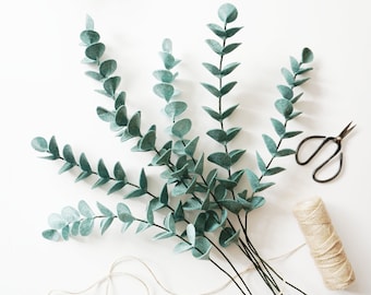 May include: A bunch of 20-inch long, faux eucalyptus stems with green felt leaves. The stems are tied together with twine and the text "20 inches/ 50cm Large Stem" is written below.