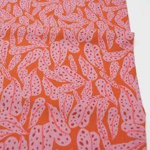Könnte beinhalten: Leuchtend orangefarbener Stoff mit einem sich wiederholenden Muster aus rosa Blättern mit dunkelrosa Punkten. Die Blätter haben eine stilisierte, organische Form und erzeugen ein lebendiges Design. Der Stoff eignet sich für Kleidung oder Heimtextilien.