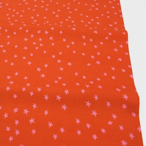 Op de afbeelding: Fel oranje stof met een herhalend patroon van kleine, lichtroze sterren. De sterren zijn gelijkmatig verdeeld over de stof, waardoor een speels en grillig ontwerp ontstaat. De stof lijkt een lichtgewicht materiaal te zijn, mogelijk katoen of een vergelijkbaar textiel.